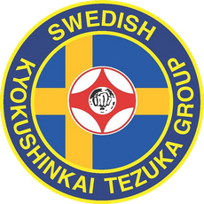 Cirkelformad logotyp för Tezuka Group Sweden, med svenska flaggan som bakgrund och symbolen för kanku med en knytnäve i mitten